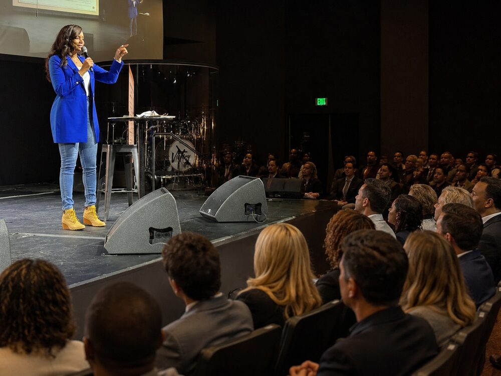 Karen in a blue blazer speaking to a full auditorium